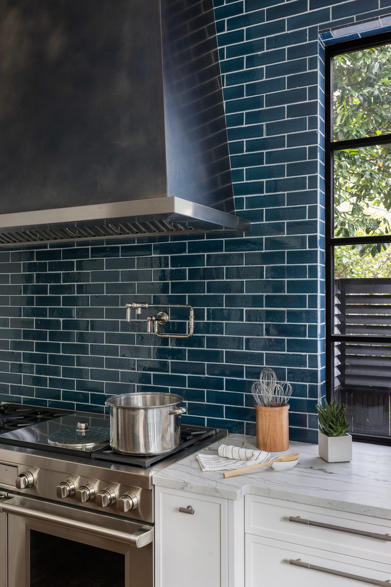Fully styled kitchen countertop vignette with a wooden utensil holder, folded linen towel, small succulent, and wooden spoon arranged with intention against a blue tile backsplash.