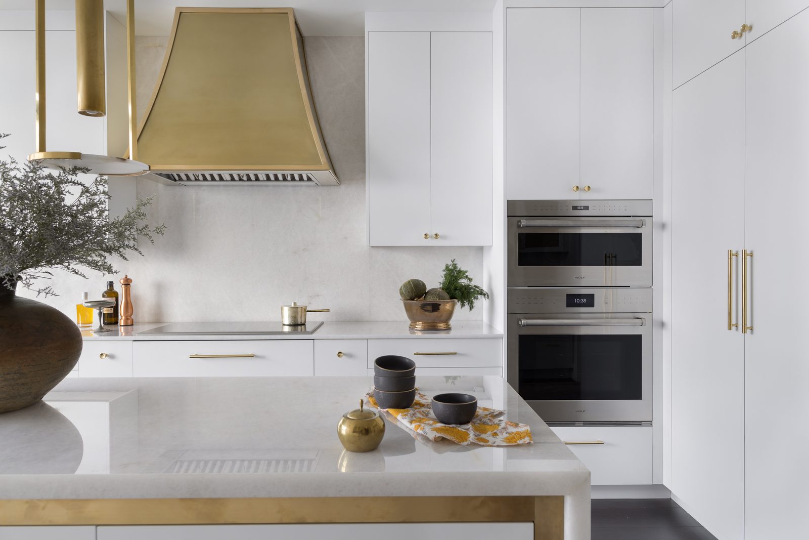 White kitchen with a brass range hood and styled marble island — a finished final delivered through an online gallery within one to two weeks of the shoot.