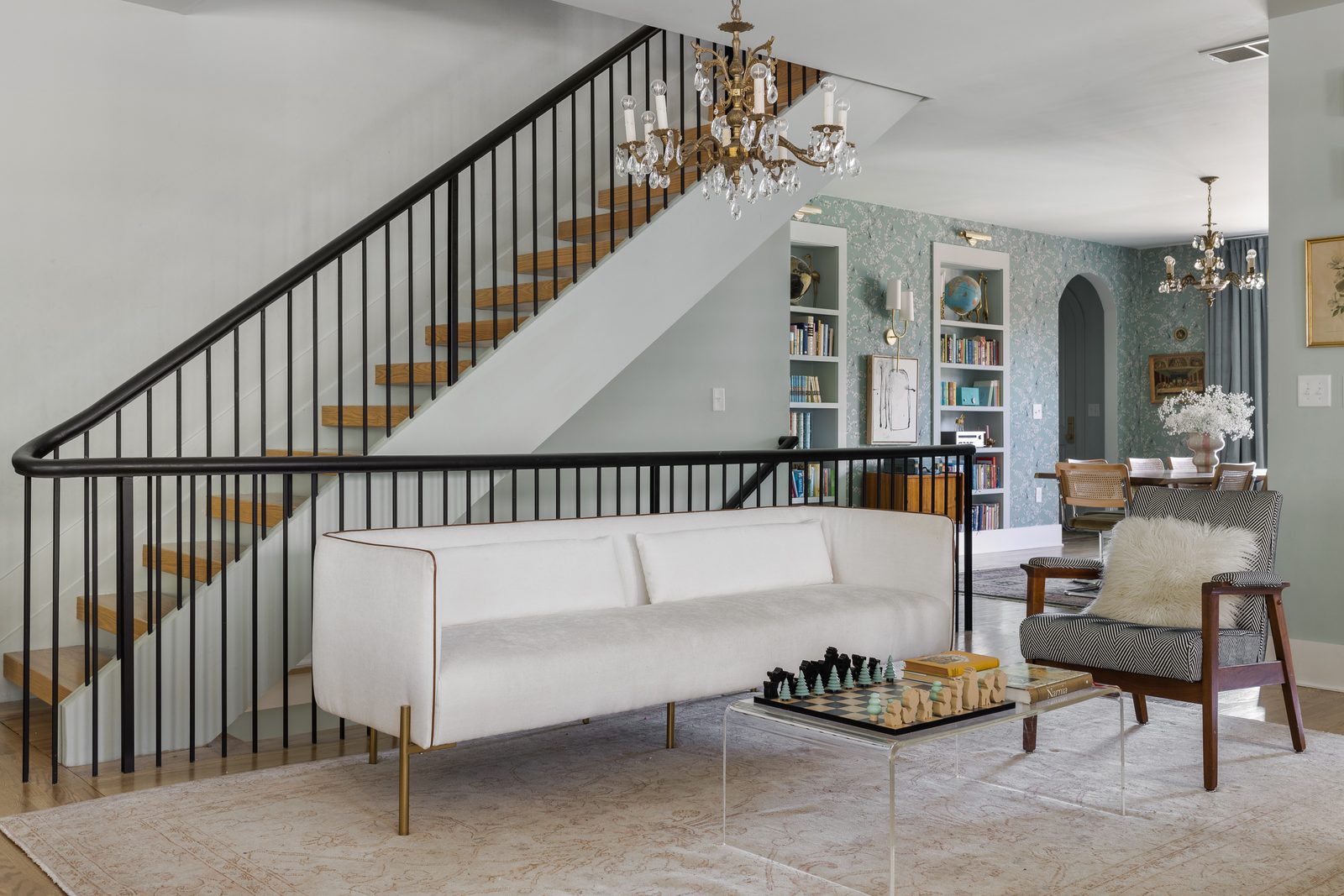 Living room at the base of a black-railed staircase with a crystal chandelier and white sofa — the kind of hero frame that takes most of an hour and a dozen micro-decisions to land.