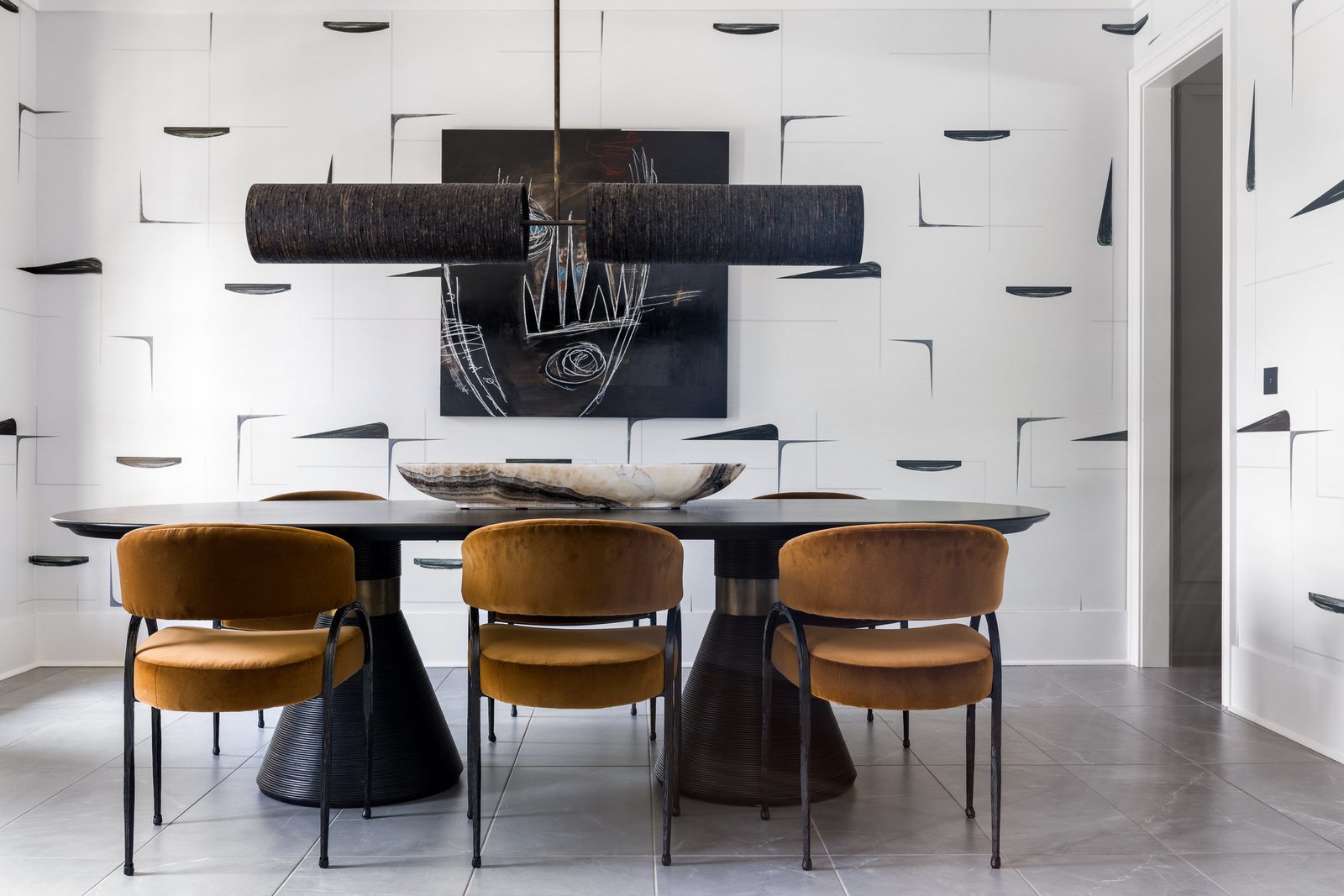 Moody dining room with graphic black-and-white wallpaper and cognac velvet chairs — the editorial finish of color grading, exposure balancing, and perspective correction carries a frame like this from accurate to published.
