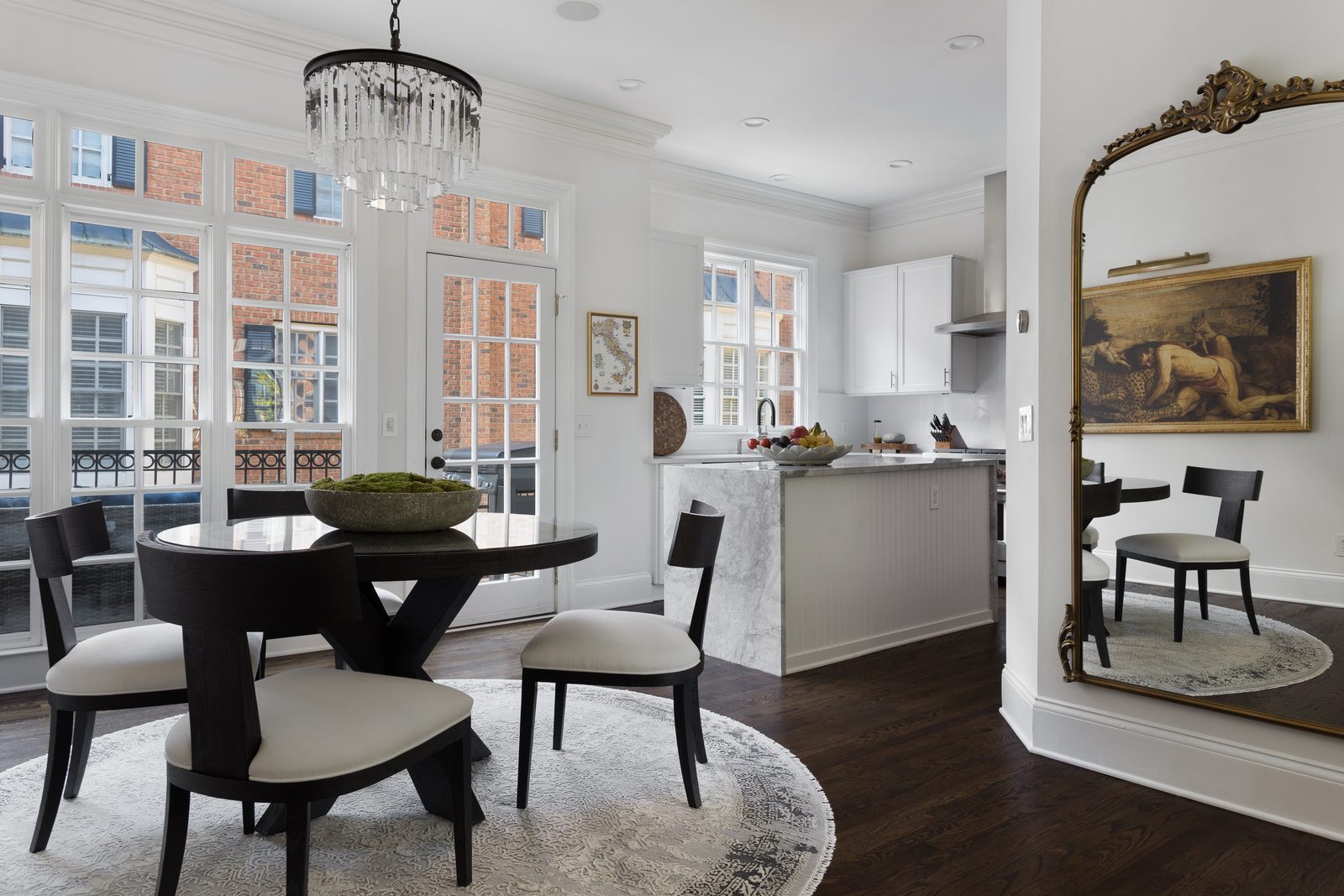 Bright dining and kitchen space with a crystal chandelier lit against tall daylight-filled windows: the exact mix of natural and artificial light this post is about.