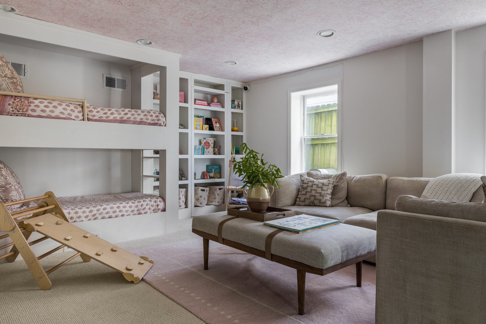 Neutral-toned bunk room and lounge with built-in beds, layered textiles, and greenery — a space styled at the depth the camera reads, not just tidied for guests.