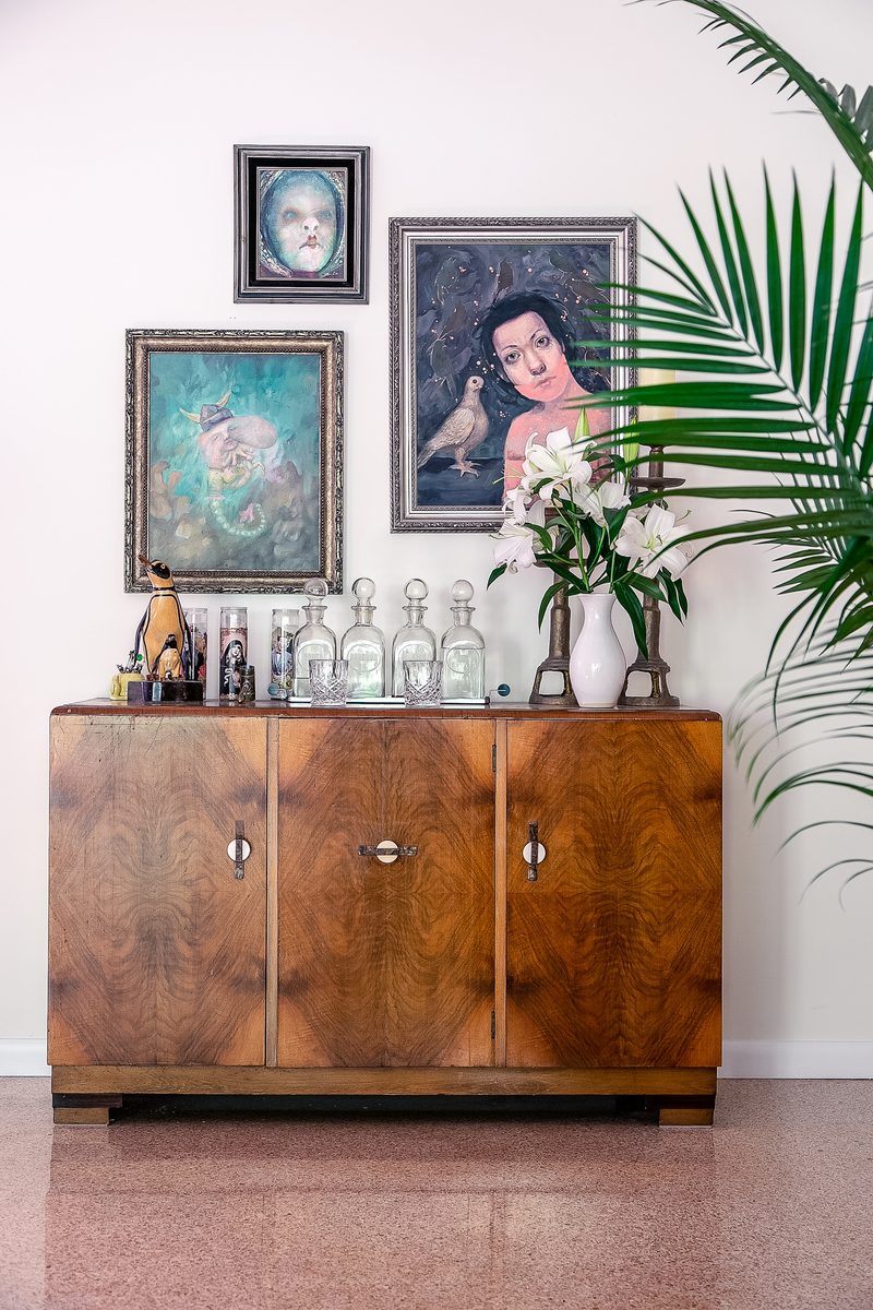 Vertical editorial vignette of a burl-wood bar cabinet styled with framed art, fresh flowers, and palm fronds — the detail frame every publication submission needs.