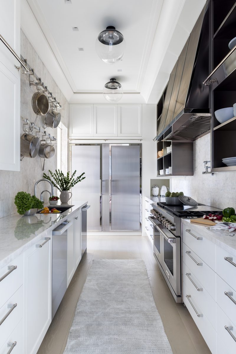 A well-designed galley kitchen left mostly as the client uses it, with real produce and herbs on the counter and pots hanging where they normally live, rather than fully art-directed.