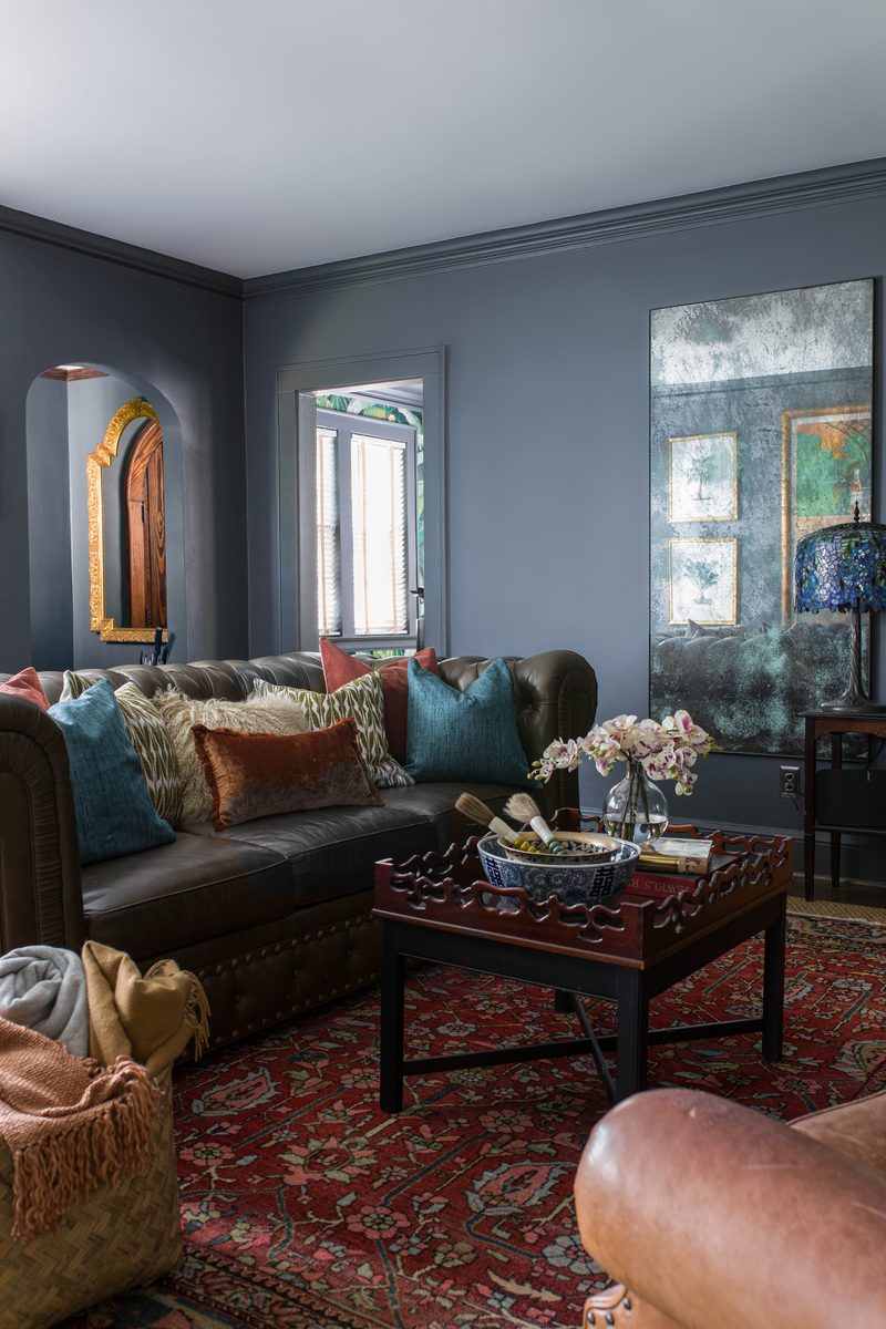 Vertical frame of a moody gray living room with a tufted leather sofa, layered pillows, and an antiqued mirror panel, the kind of vertical that earns one slot on the project page and several on the grid.