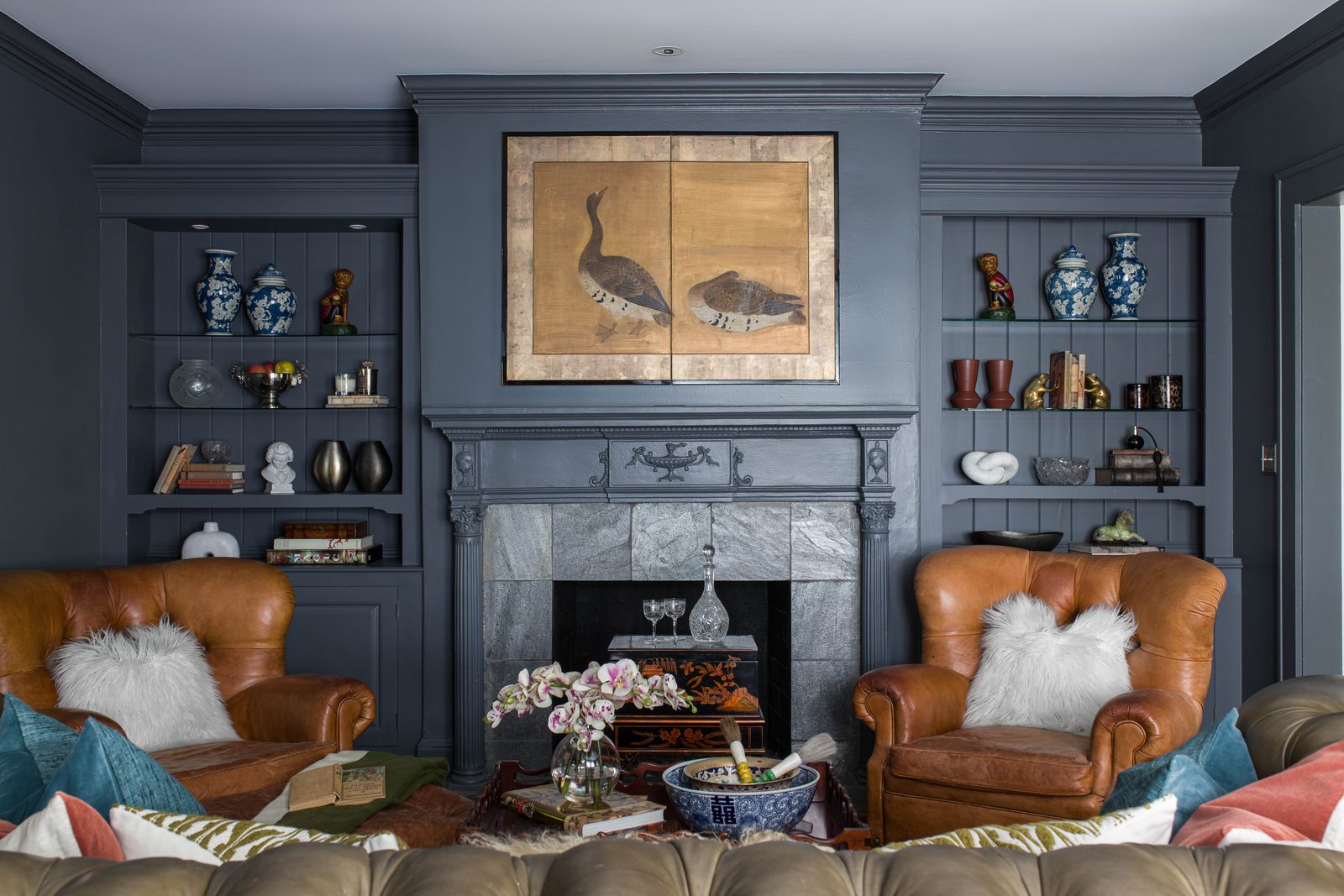 Wide editorial frame of a navy living room with built-in shelving, a slate fireplace, and a pair of leather armchairs, the establishing shot that anchors a website project page.