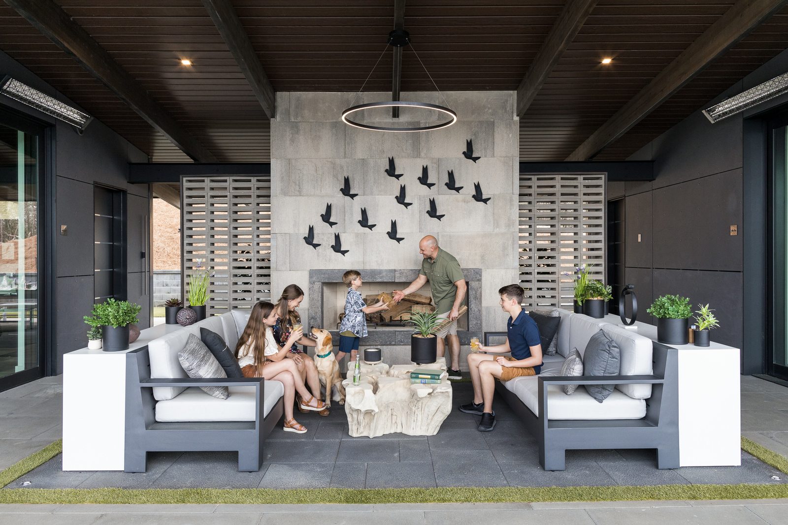 A real family gathered around an outdoor fireplace with their dog, genuinely interacting rather than posed for a product shot: the lived-in end of the styling spectrum.