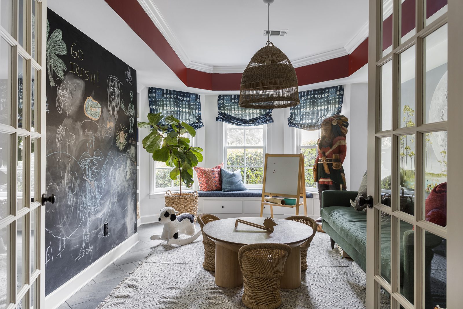 An unstaged kids' playroom with a chalkboard wall full of real drawings, a stuffed toy on the floor, and a child-sized craft table left exactly as the family uses it.